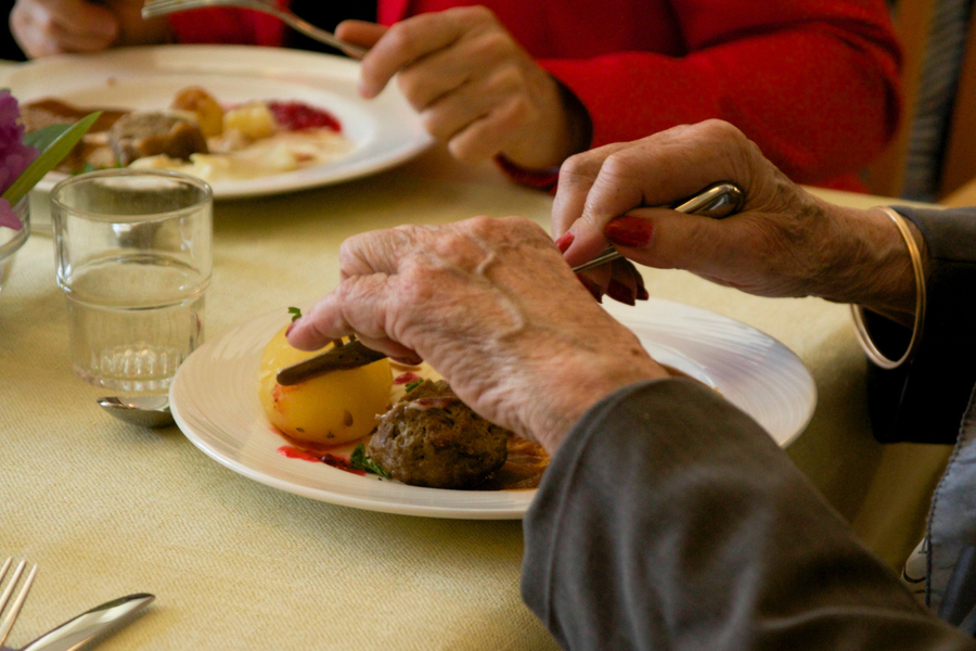 En närbild på händerna på två äldre kvinnor som sitter jämte varandra och äter middag.