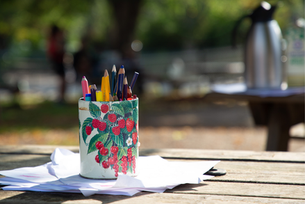 En närbild på en blommig burk med färgpennor i som står ute på ett bord i solsken.