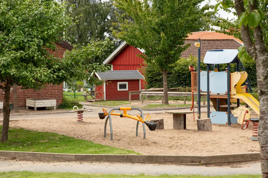 En lekpark omgiven av lummig grönska. I bakgrunden skymtas Öxabäcks förskola.