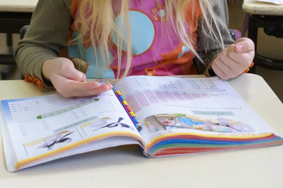 En närbild på händerna på en flicka som sitter vid en skolbänk med en mattebok och räknar på fingrarna.